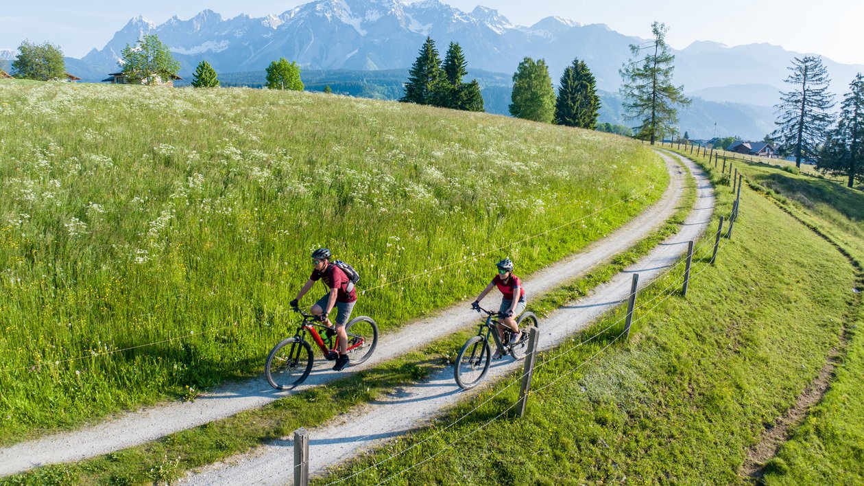 Bergabenteuer auf zwei Rädern Zwei Radfahrer fahren einen gewundenen Pfad in einer grünen Landschaft mit Bergen im Hintergrund.