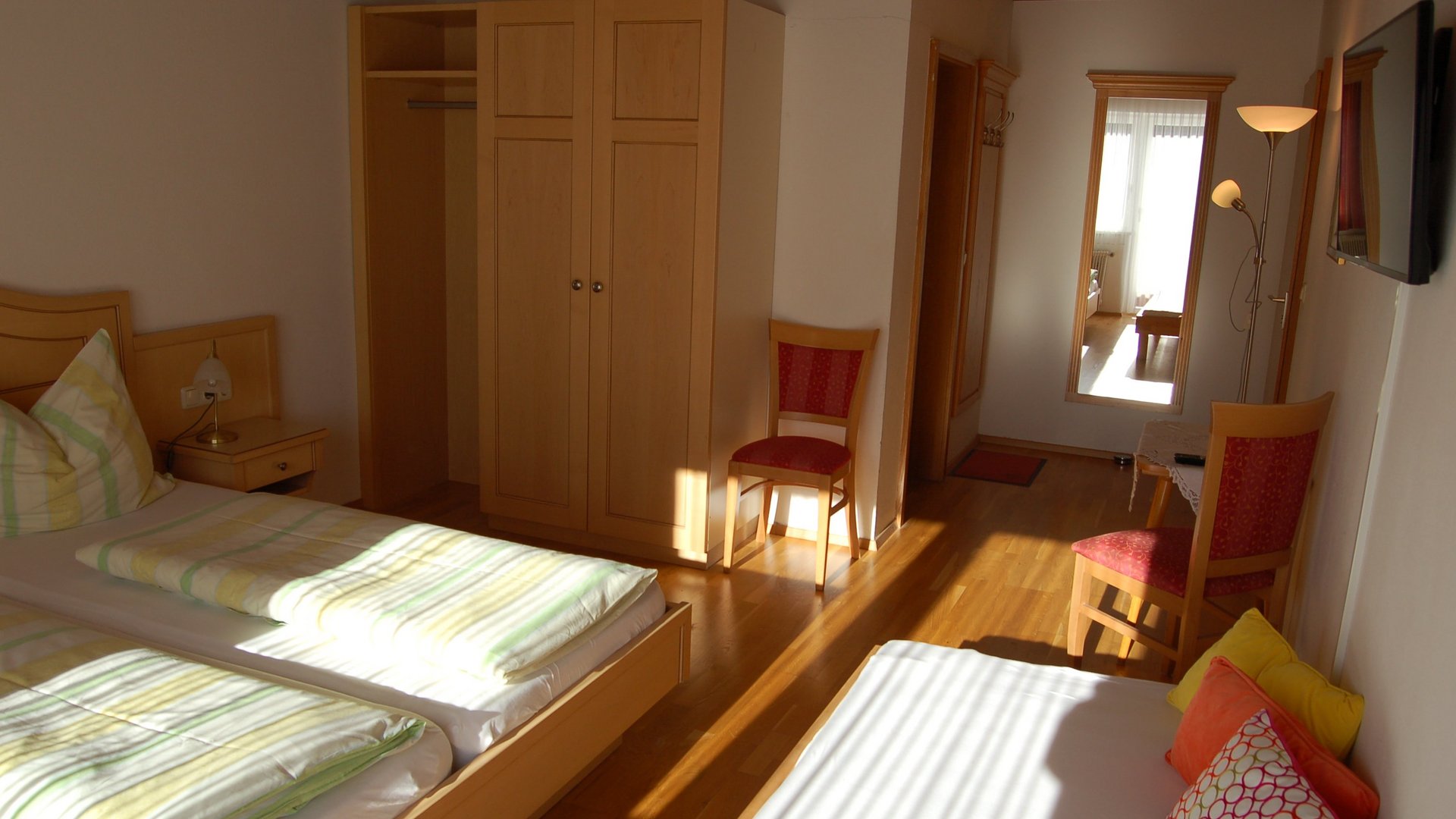 Modernes Hotelzimmer mit Holzdetails Hotelzimmer mit zwei Betten, einem Kleiderschrank, einem Stuhl und einem Spiegel auf Holzboden