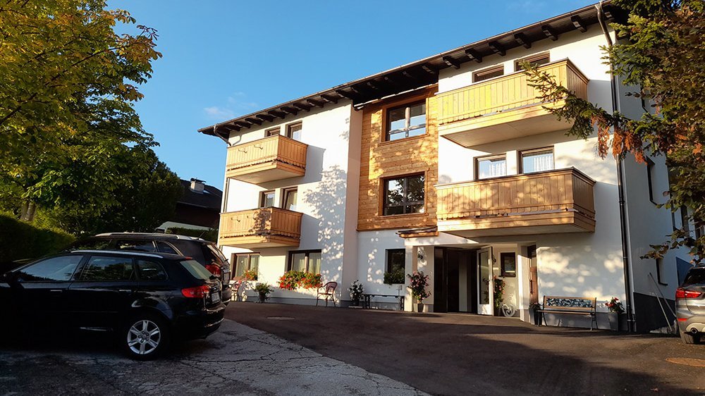Moderne Wohnarchitektur in Schladming Dreigeschossiges Wohngebäude mit Holzbalcon und umgebender Landschaft und Bäumen